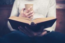 Mann mit Kaffeebecher vorm offenen Buch